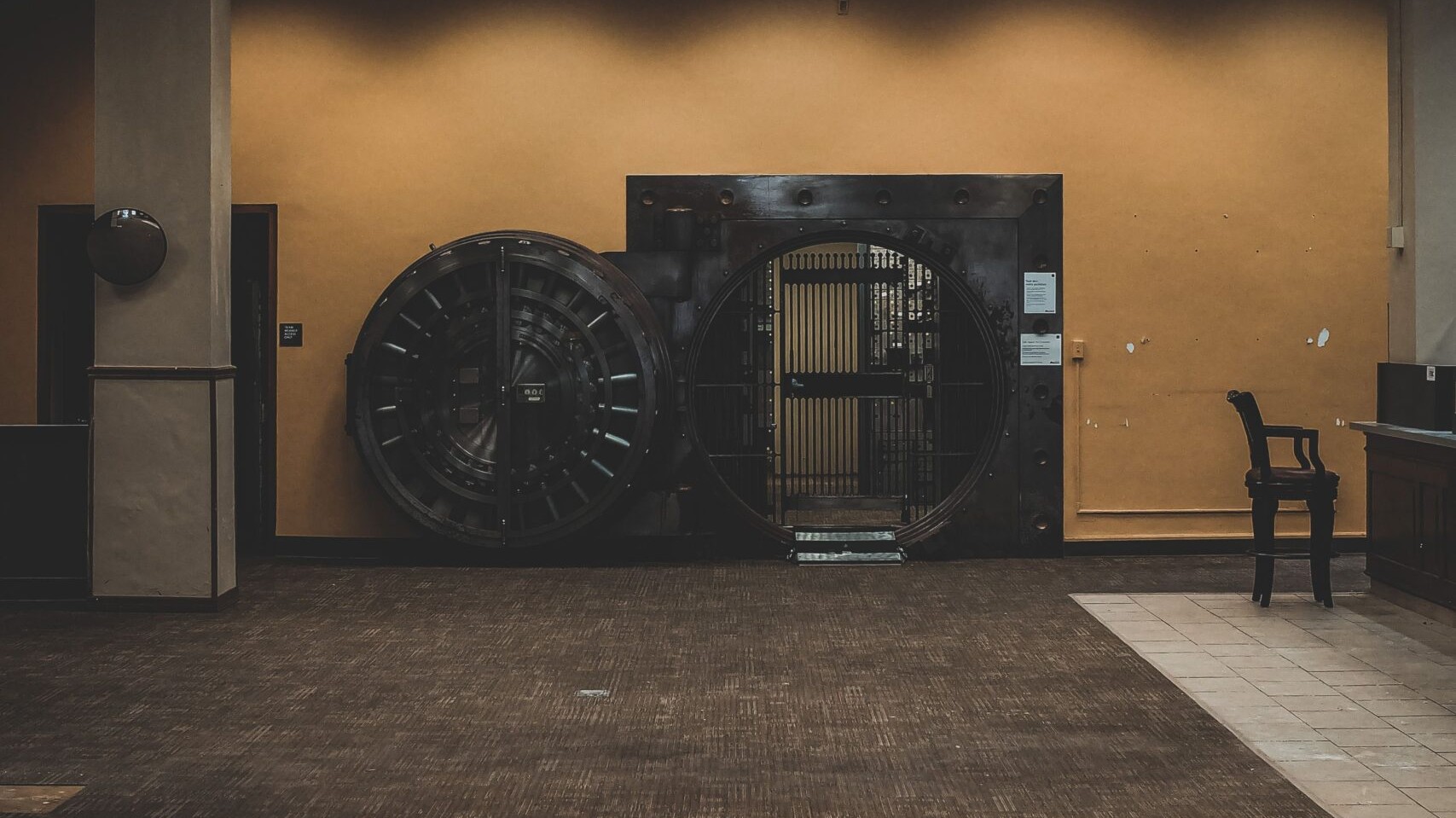 A large, open circular bank vault door in an old bank interior, standing in for the vault a password manager keeps your credentials in.